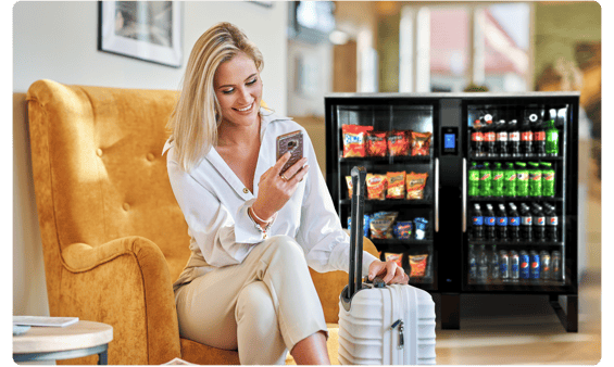 A professional woman traveling with luggage seated in a hotel lobby with a Stockwell as a convenient self-service option for a snack or drink